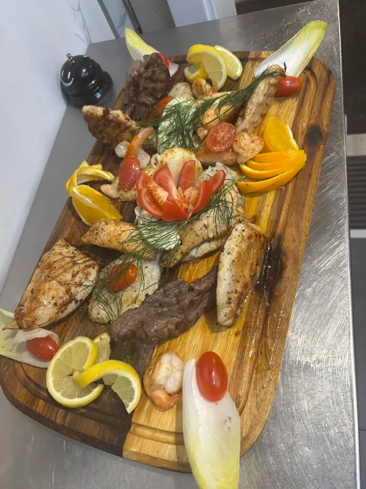 Grillplatte auf Holzbrett mit Fleisch, Fisch, Gambas und Zitronen